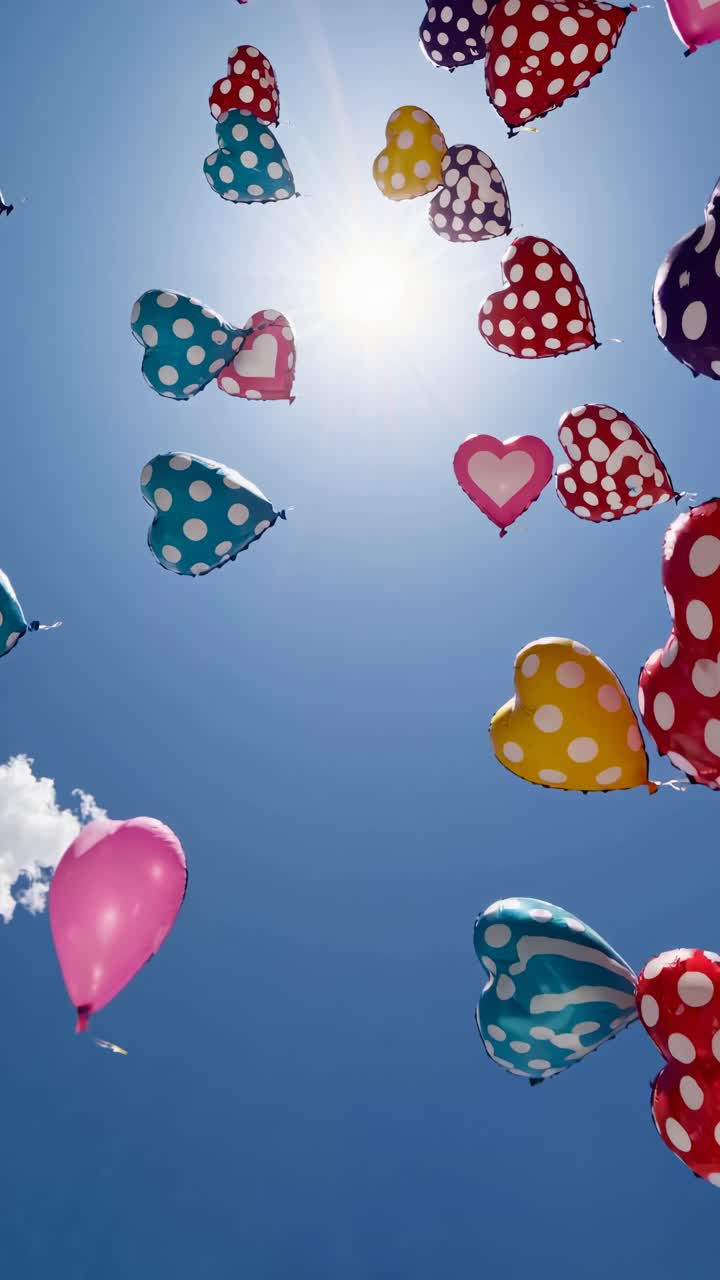 Video con angolazione verso l'alto di palloncini colorati a forma di cuore su un cielo blu brillante