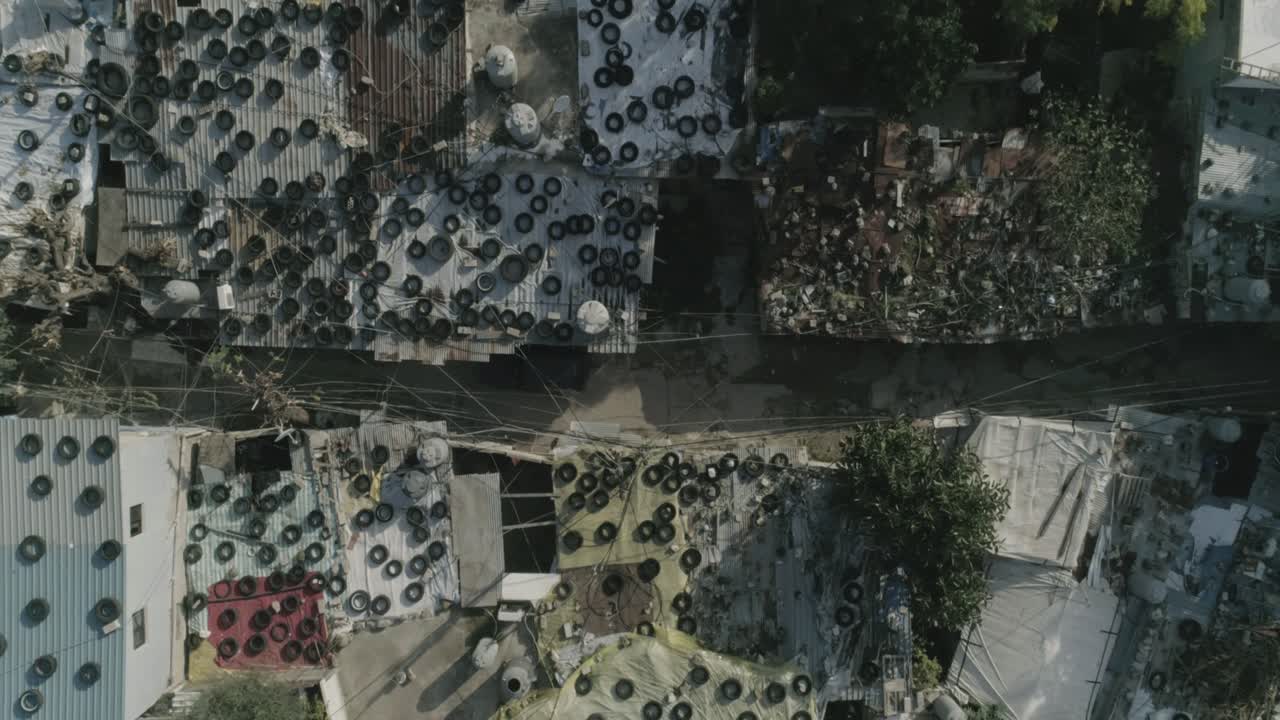 Aerial top-down panning view over improvised roofs with tyres of Palestinian refugees camp