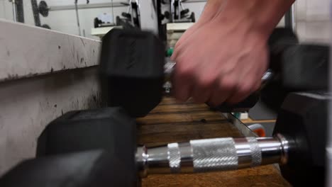 male hands picking up dumbbell from gym bench