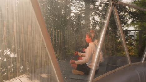 woman and man practice yoga in lotus poses. couple intertwines body and mind among serene resort. view through glamping glass terrace. embracing profound tranquility