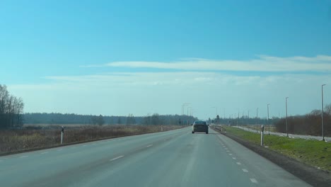 fpv or first person view from inside a car driving forward on a aspahalt road with white marking on a sunny summer day in harku estonia, blue sky, trees and farm fields visible on the sides and above.