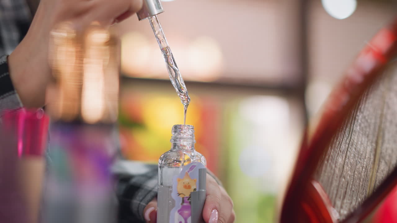 Closeup partial view of lady's hand holding serum dropper, watching liquid drip into bottle, skincare product in focus with blurred background, capturing elegance and beauty care routine in detail