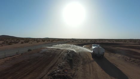 Ein-Wassertankwagen-Spritzt-Vor-Dem-Motorradrennen---Luftbild---Einen-Offroad-feldweg-Hinunter