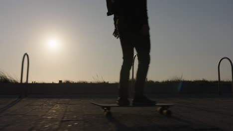 silueta en cámara lenta de un patinador patinando a lo largo del paseo marítimo durante la puesta de sol dorada en el mar de los países bajos