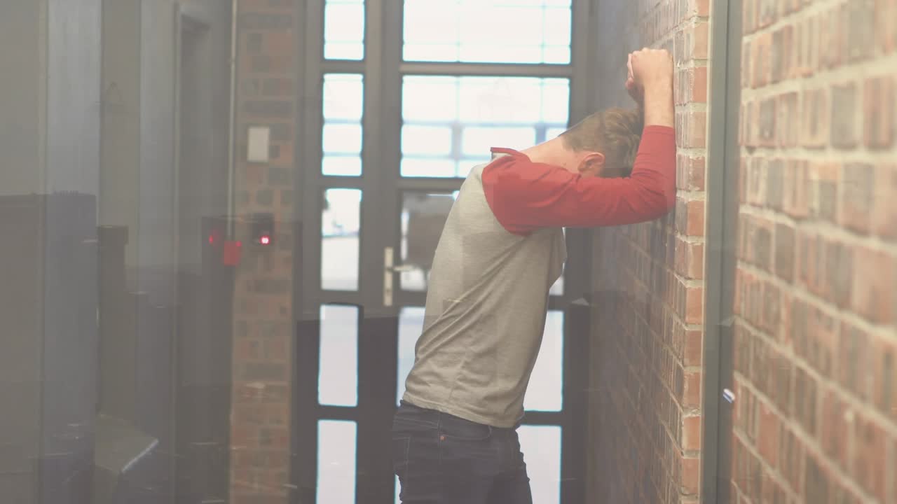 Lavoratore maschio frustrato che batte contro il muro nel corridoio dell'ufficio, con paesaggio urbano sullo sfondo