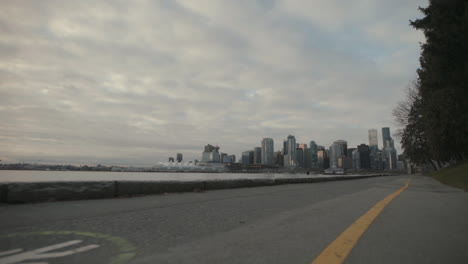 Wide-low-angle-shot-of-Seawall-trail-with-Vancouver-skyline-in-background,-Morning,-Slowmo