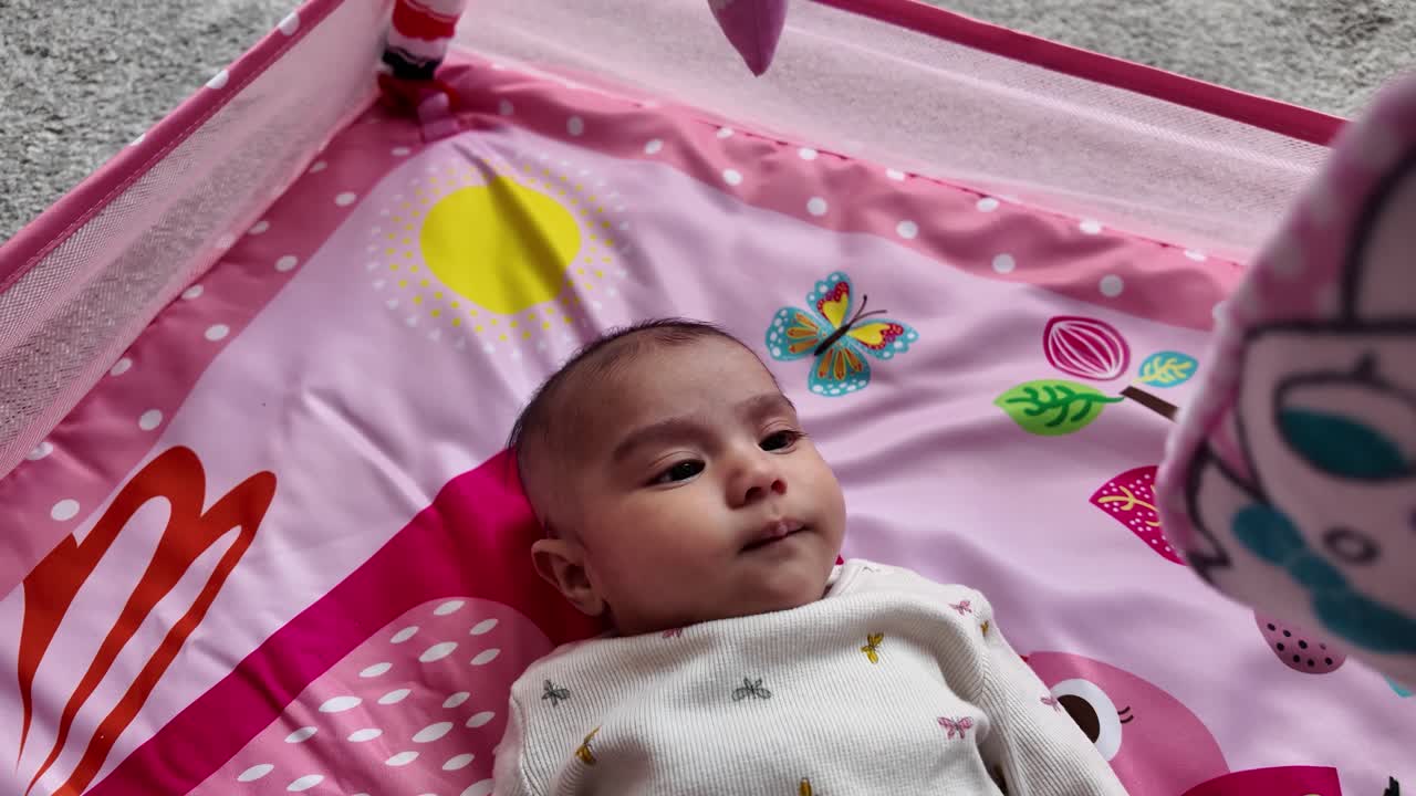 Adorable three month old baby girl lies on a pink play mat, enjoying her playtime. slow motion