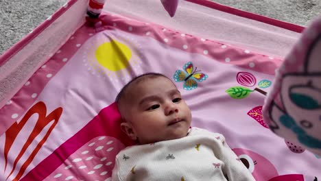 adorable three month old baby girl lies on a pink play mat, enjoying her playtime. slow motion