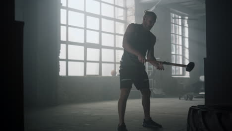 Sportsman-hitting-tire-with-hammer-in-gym.-Man-exercising-with-sledgehammer