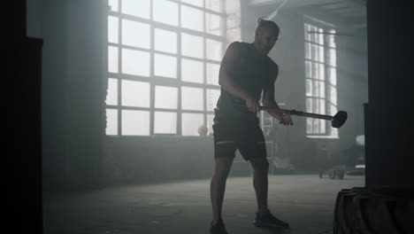 sportsman hitting tire with hammer in gym. man exercising with sledgehammer