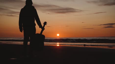 hombre corriendo con guitarra en la playa de arena trasera al atardecer-14