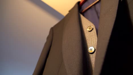 a men's blazer hanging on a wooden hanger, below it is a gray waistcoat