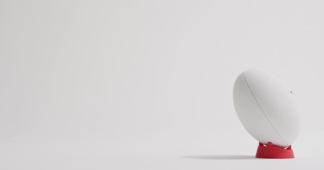 White rugby ball on kicking tee on white background with copy space, slow motion