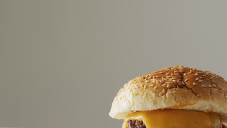 video close up of cheeseburger with salad in burger bun, on pale grey background with copy space