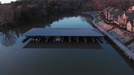 aerial drone footage flying over calm water and boat docks with nice houses on the right at sunset