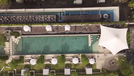 aerial top-down shot of a hotel rooftop swimming pool at a luxury resort in bali, indonesia, showcasing crystal-clear water, modern architecture, and a serene tropical ambiance.