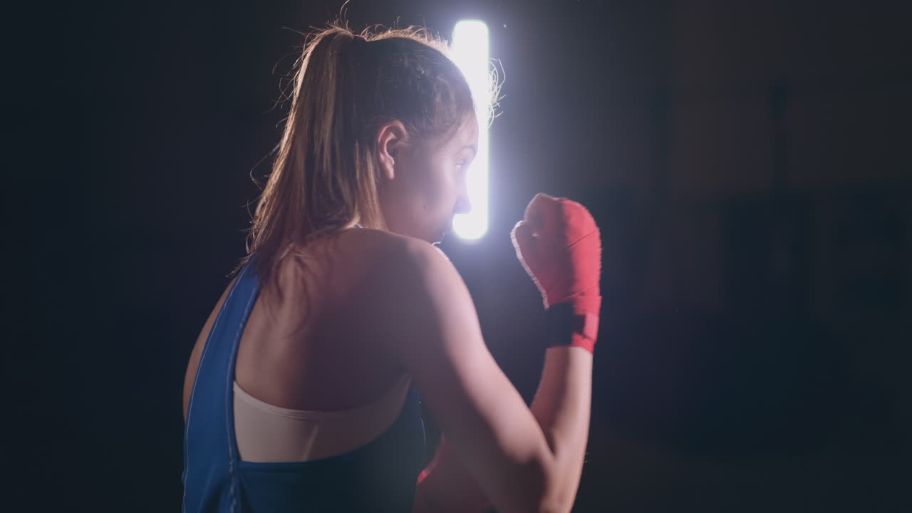 Beautiful woman fighter in red bandages conducts a shadow fight while exercising in the gym. Slow motion. steadicam shot
