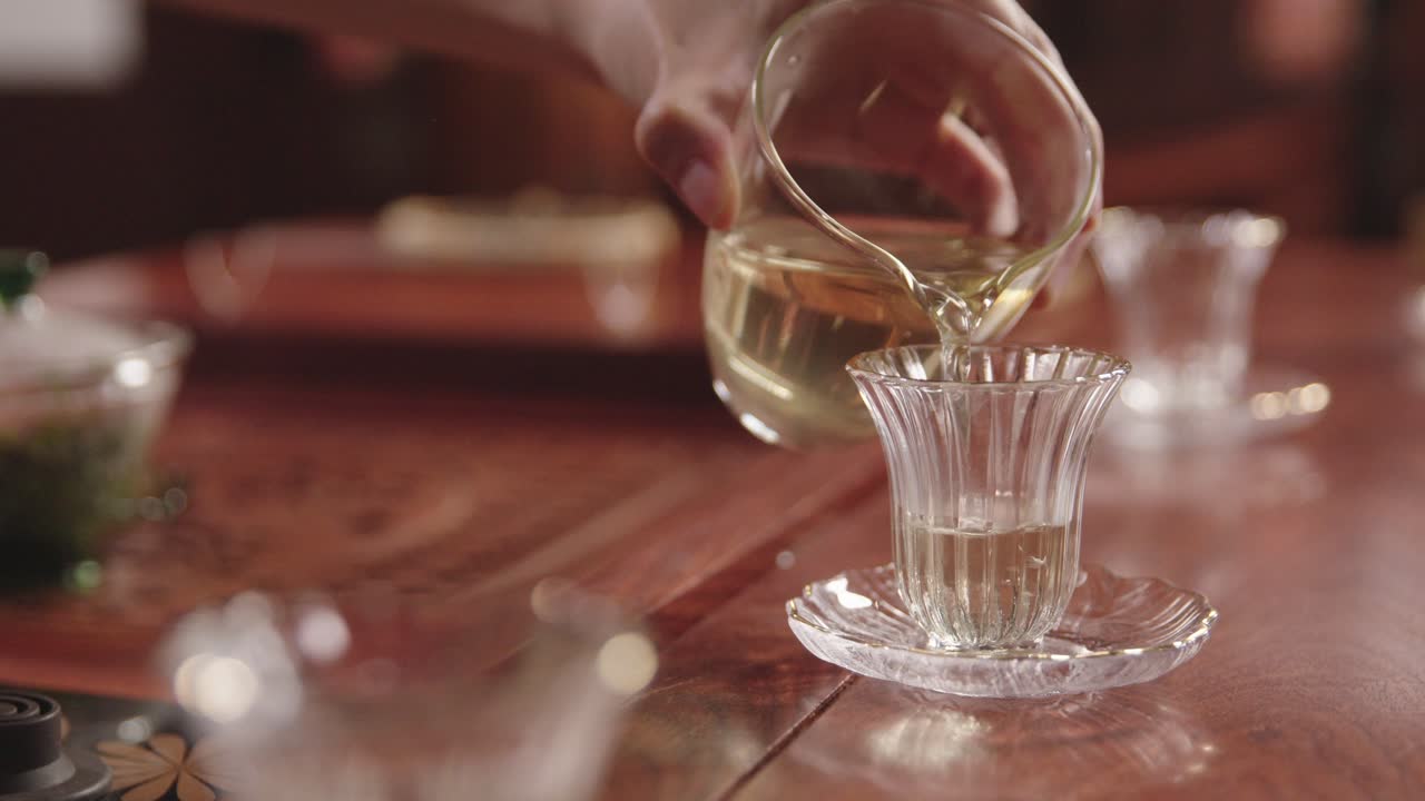 중국 여성은 갓 준비한 녹차를 전통적인 어두운 나무 티 테이블에 있는 유리 컵에 붓는다