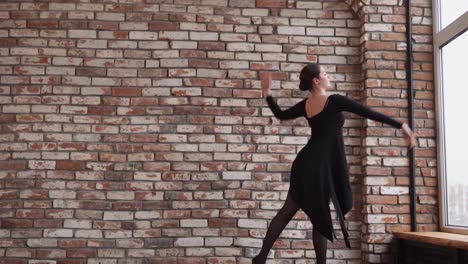 bailarina de ballet en un vestido negro por una pared de ladrillo