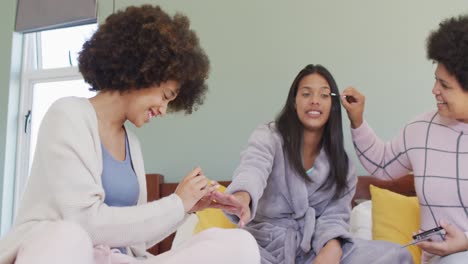 happy diverse female friends doing make up and smiling in bedroom