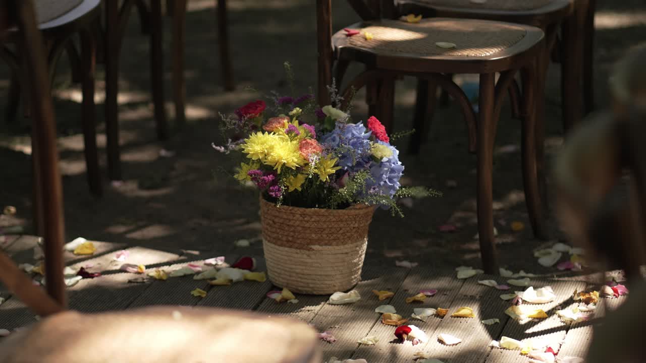 Colorful flowers in a woven basket with scattered petals at a rustic wedding