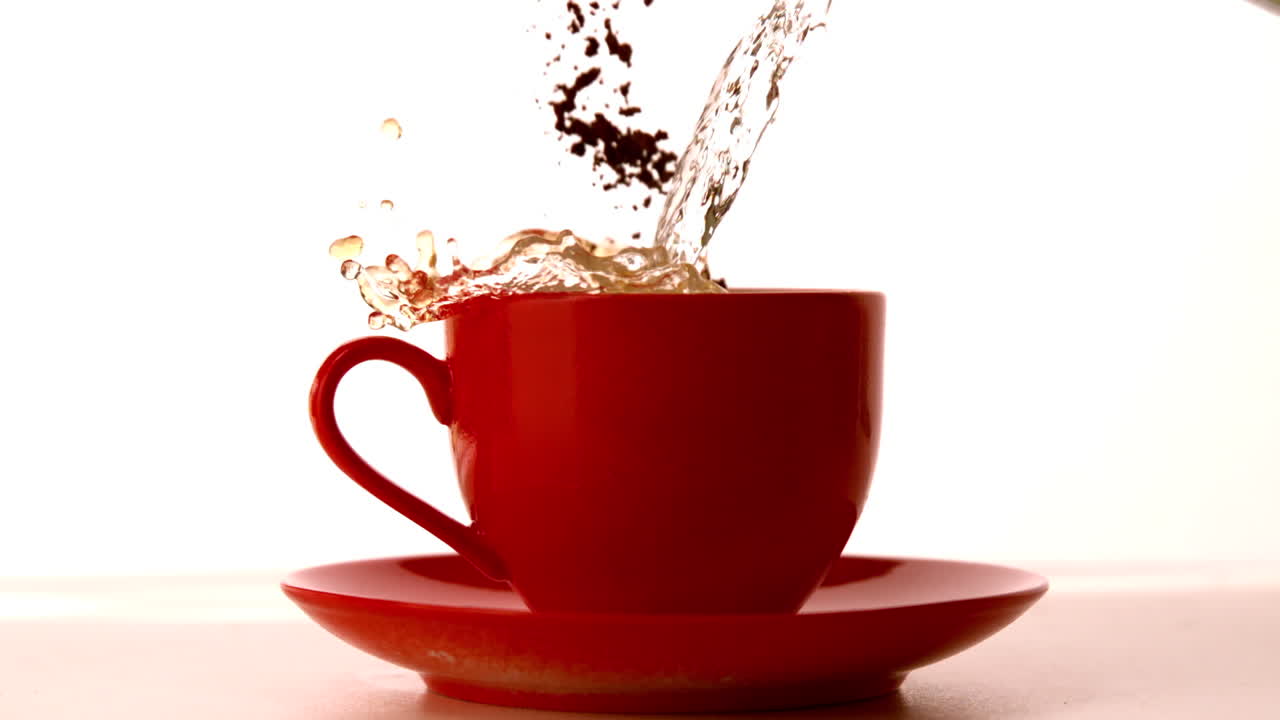 Granuli di caffè e acqua che cadono in una tazza rossa