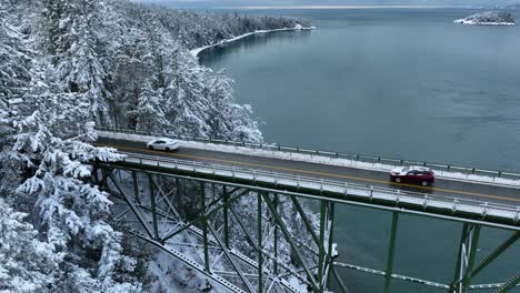 Statische-Drohnenaufnahme-Von-Autos,-Die-Eine-Stahlbrücke-Verlassen-Und-Das-Schneebedeckte-Festland-Betreten