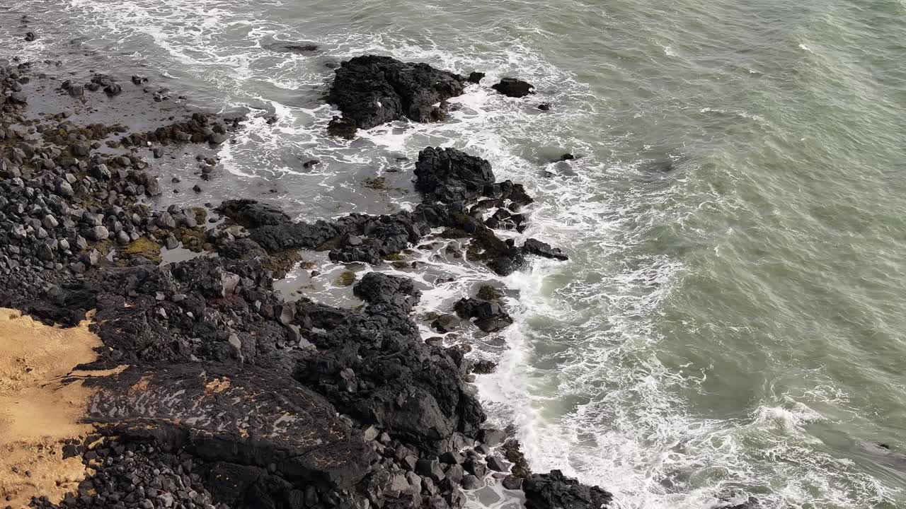 Aerial view of Iceland's rugged Búðakirkja coast in Búðir, Snæfellsnes. Black volcanic rocks meet the Atlantic waves beside golden sand in a dramatic natural contrast.
