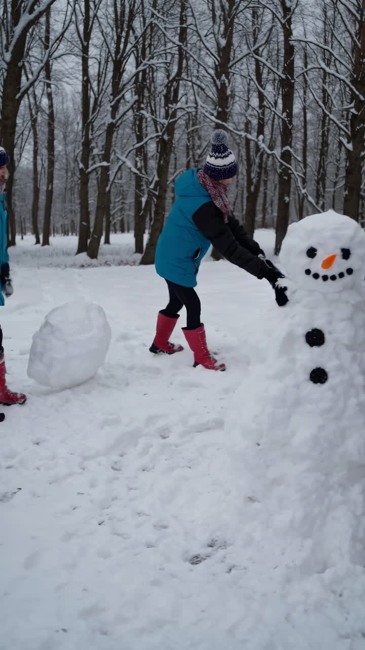 A group of friends builds snowmen in a snowy forest. Captured from a low angle, the video showcases