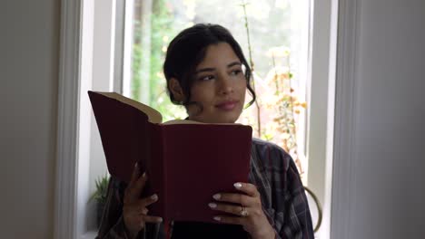 Niña-Puertorriqueña-Leyendo-La-Santa-Biblia-Reflexionando-Sobre-Las-Escrituras-Religiosas-Frente-A-Una-Ventana-Brillante