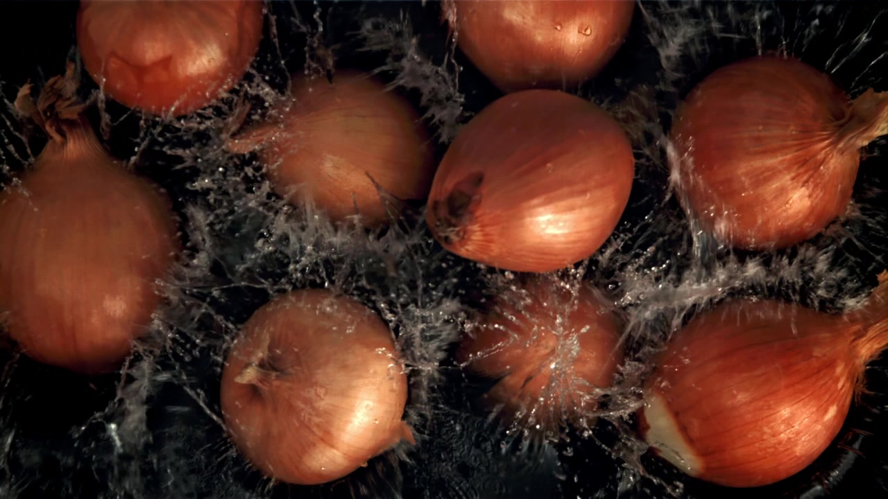 Cebollas frescas salpicando en el agua sobre un fondo oscuro en cámara lenta