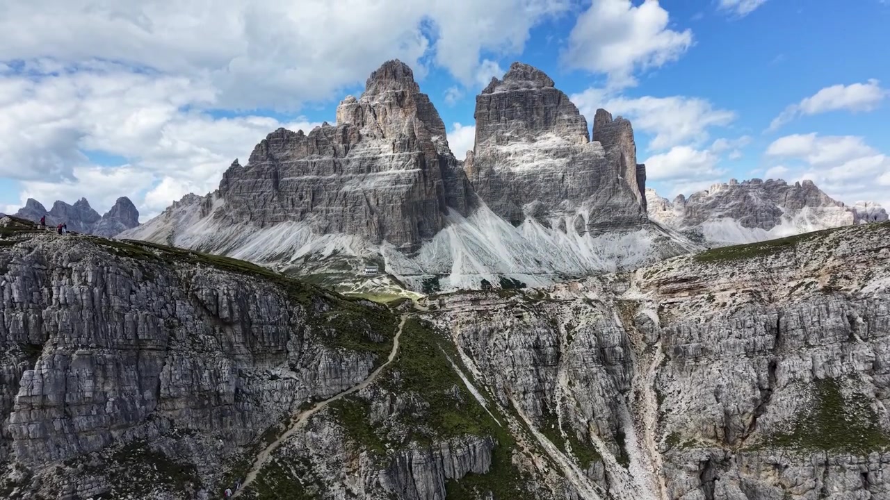 Rivelazione lenta verso l'alto con drone delle iconiche Tre Cime di Lavaredo che emergono sopra aspre scogliere calcaree nelle Dolomiti, Italia