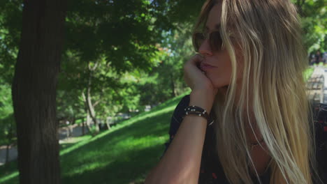 Dreamy-Blonde-Young-Woman-Rests-Her-Chin-in-Her-Hand-Sat-in-Shade,-Handheld-Shot,-Copyspace