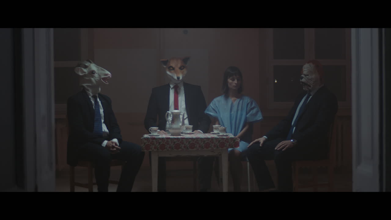 A girl sits at a table with strange figures in animal masks