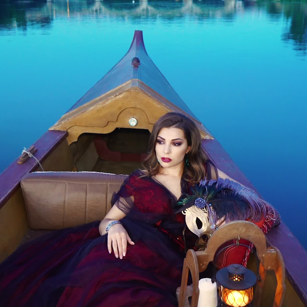 A charming woman in a red dress is riding in the gondola in the evening. Carnival in Venice. Blue background