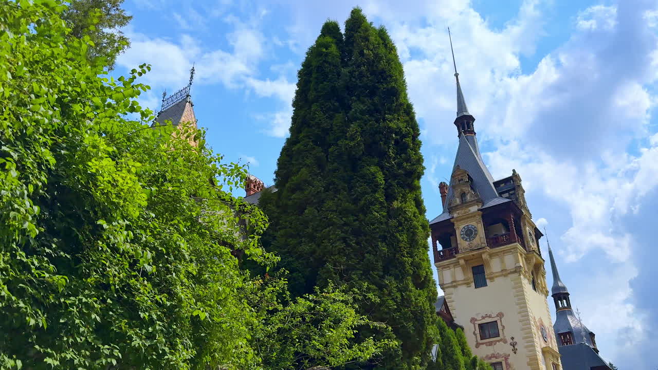 Amazing towers with steeples of the Peles Castle in Sinaia, the Carpathians, Romania. Green trees grow near the building. Low angle view