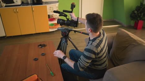 studio guy adjusting camera lens and preparing gear for video shoot in home studio. lighting, microphone, and camera equipment are carefully set up for upcoming production