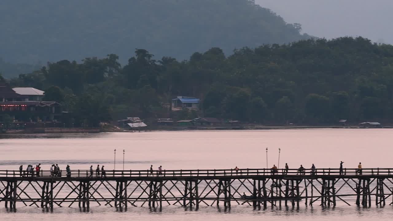 mon bridge y una lancha siguieron a toda velocidad detrás de la estructura mientras la gente caminaba por el puente, dibujando siluetas mientras oscurecía, en cámara lenta