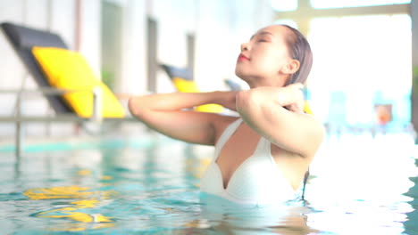 a close-up pretty young woman swimming in an indoor resort pool pushes her wet hair back away from her face