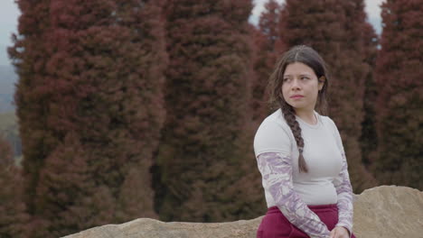 a young woman seems slightly down in the dumps as she looks around the park, all by herself