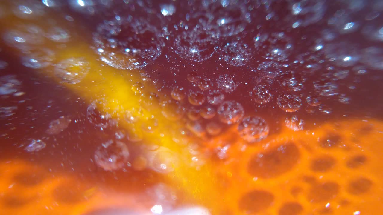 Macrofotografia di gocce di rugiada sulla superficie dell'olio e la luce del sole che si riflette splendidamente con la texture arancione