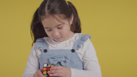 Studio-Portrait-Of-Young-Girl-On-ASD-Spectrum-Solving-Puzzle-Cube-Against-Yellow-Background-2