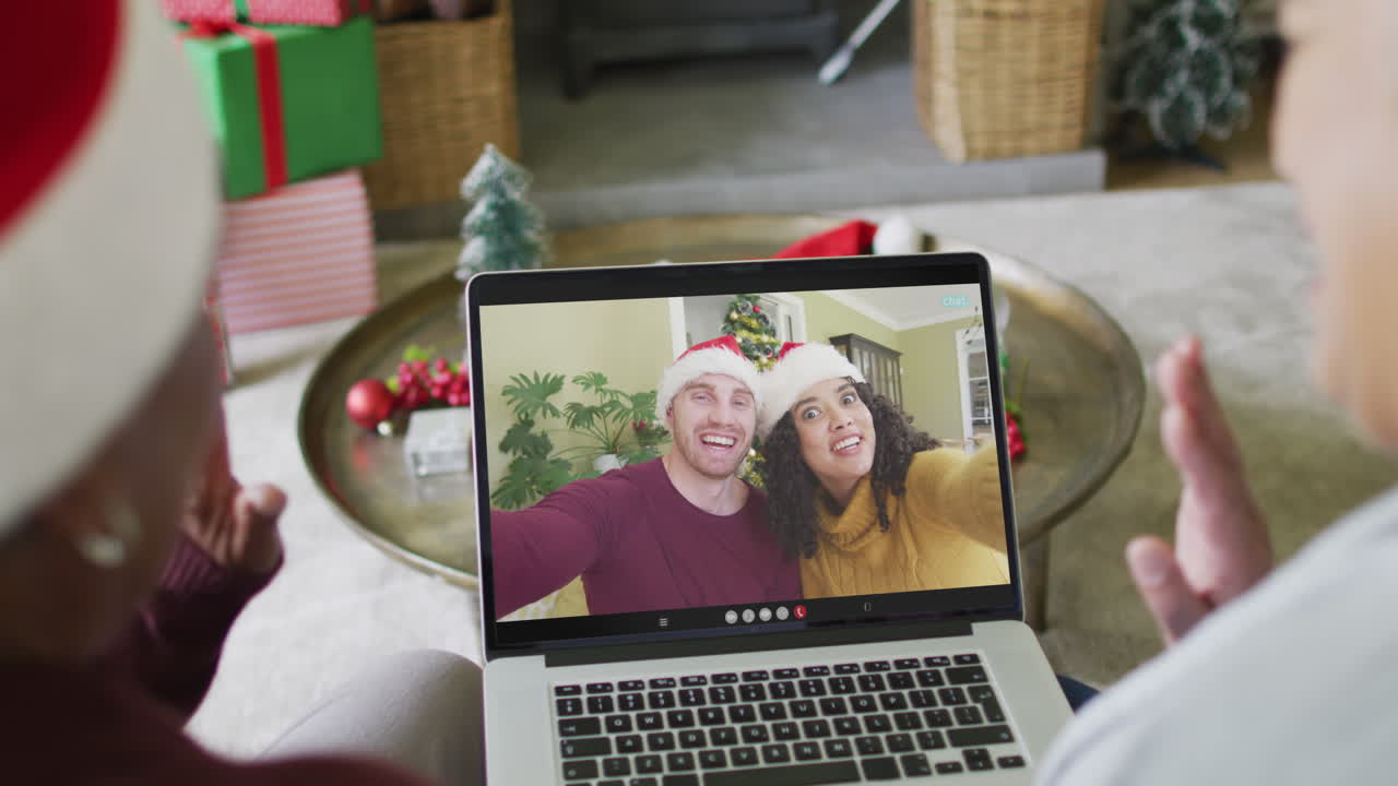diversas amigas mayores que usan una computadora portátil para una videollamada de navidad con una pareja sonriente en la pantalla