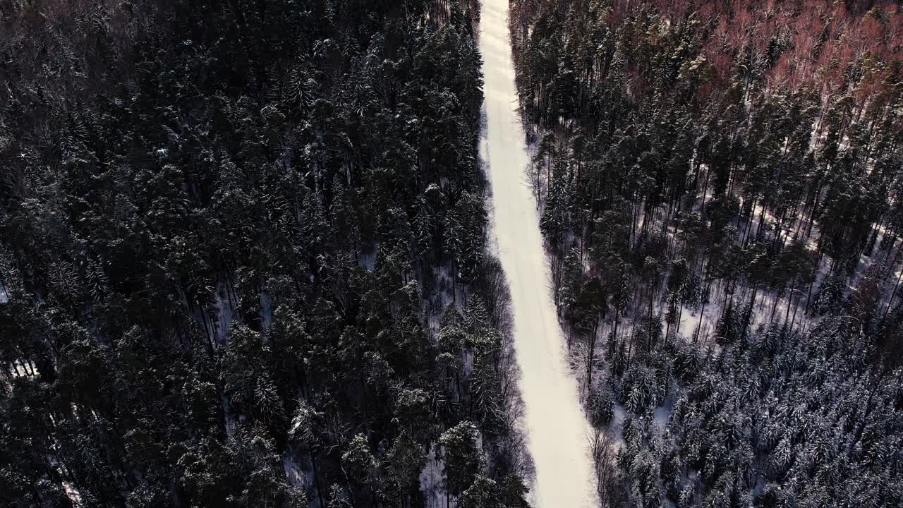 Aerial view of a drone flying over a forest road in winter