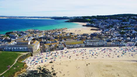 scenic town of st ives in cornwall with panning drone shot with porthmeor beach and tourists sunbathing