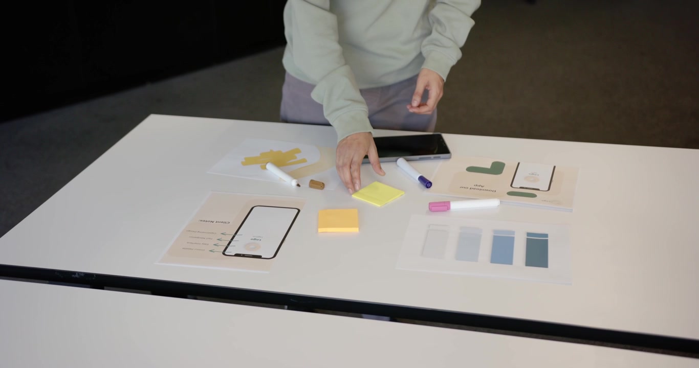 Designer africano non binario che, dopo aver posizionato un mockup di tablet, scrive su post-it e pianifica alla scrivania