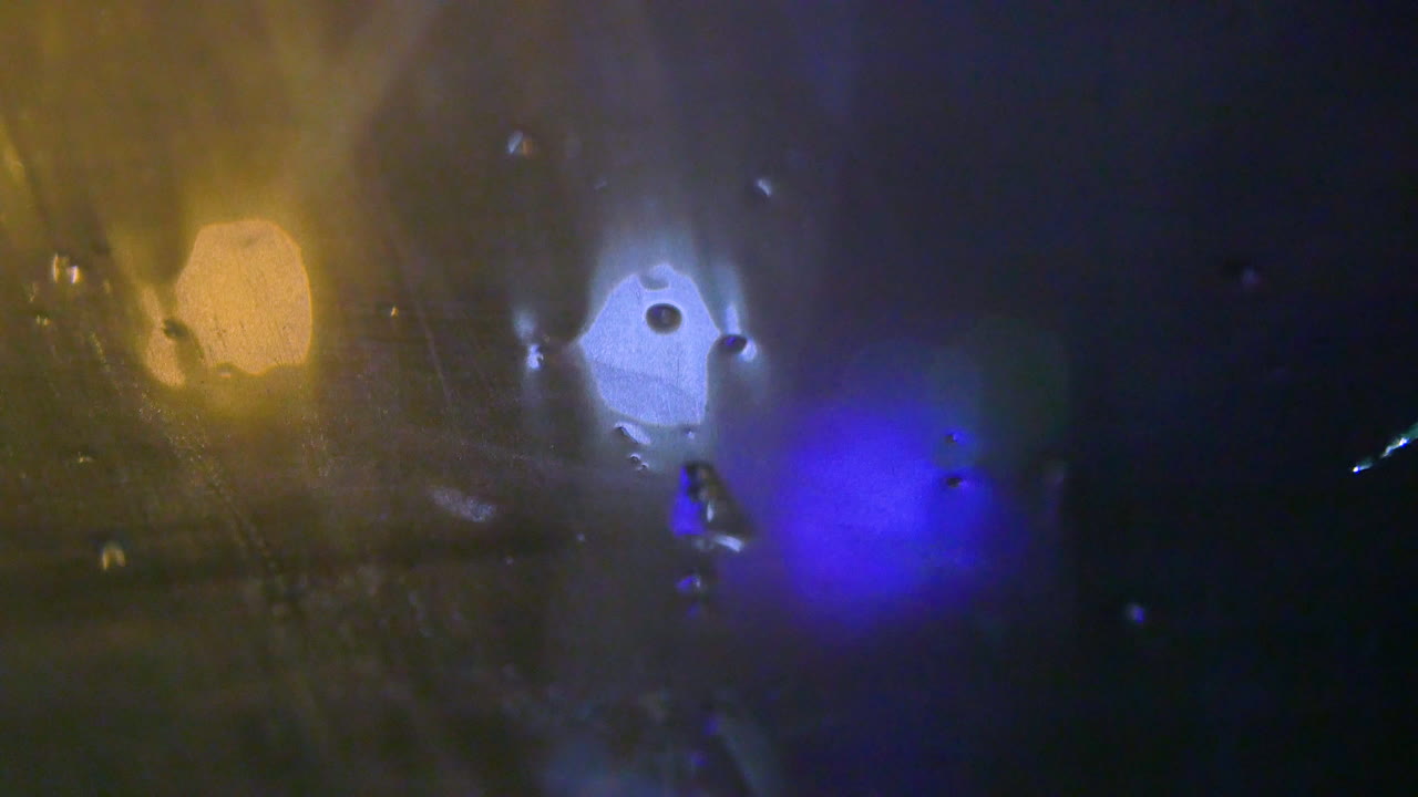 las luces de color naranja, azul bebé y cobalto brillan en la distancia mientras la nieve y la lluvia caen sobre el vidrio mojado durante una noche de invierno.