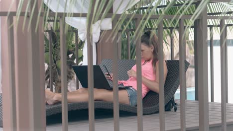 woman with laptop lies on cozy sofa at wooden terrace