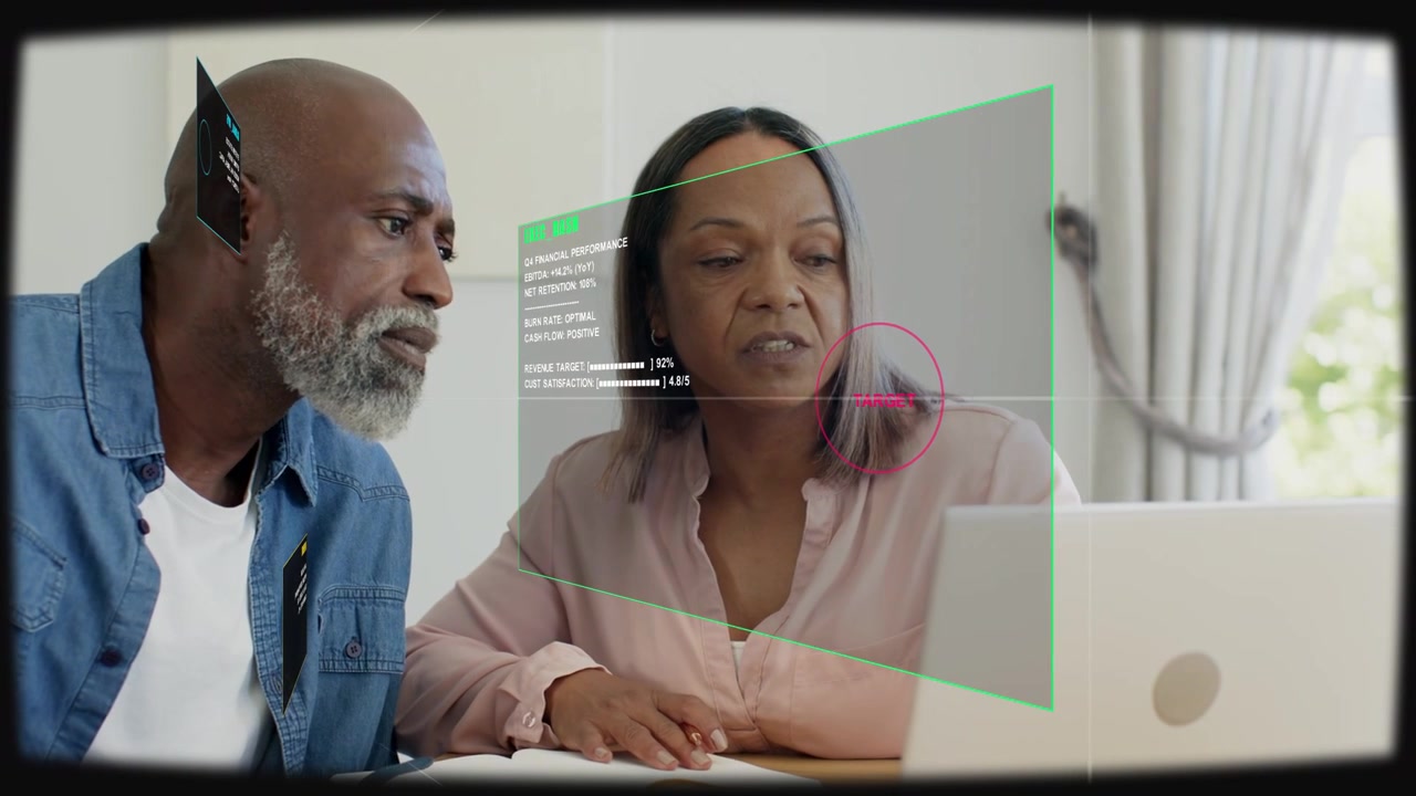 Pair sitting, woman pointing, laptop getting pink target and green HUD overlay while managing bills