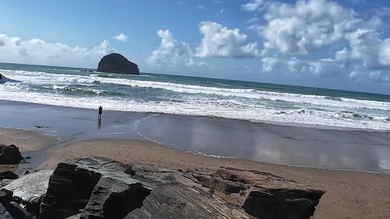 Aerial view of Trebarwith Strand's rugged coastlines, with azure waves and rocky cliffs under vibrant skies. Sparse beachgoers add life to this sunlit Cornish paradise